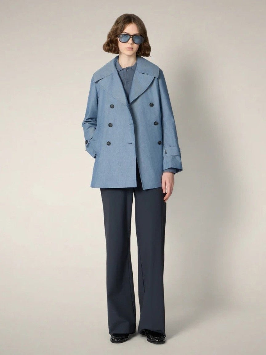 A person wearing dark sunglasses, the SAVE THE DUCK SELA Peacoat Raincoat in Chambray, and wide-leg dark pants stands against a plain light background.