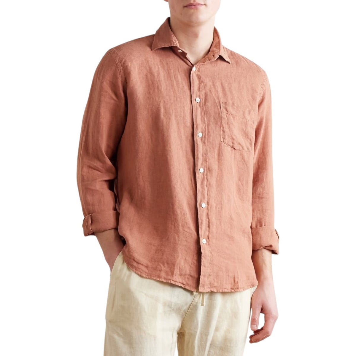 A person wears the HARTFORD - PAUL LINEN SHIRT IN FADED COPPER by HARTFORD, paired with light pants, standing with one hand in their pocket against a plain background.