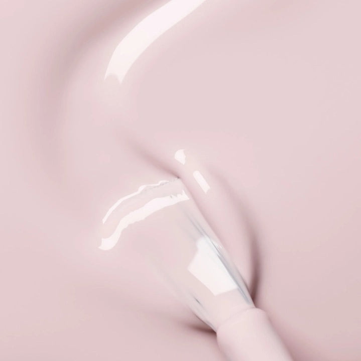 A hand with pale pink polished nails holds a bottle of MANUCURIST INC GREEN™ Nail Polish in Blossom against a gray knit sweater background.