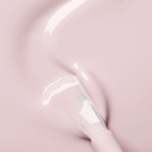 A hand with pale pink polished nails holds a bottle of MANUCURIST INC GREEN™ Nail Polish in Blossom against a gray knit sweater background.