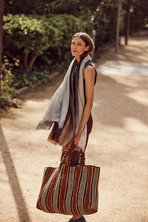 The GABRIELE FRANTZEN Raffia Weekender Bag Tobacco is a large, handmade bag with two handles and vertical stripes in brown, tan, cream, and gray for a textured, artisanal look.