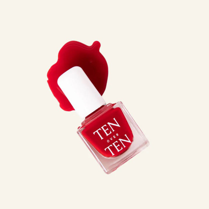 A glass bottle of TENOVERTEN - NAIL POLISH from the brand TEN OVER TEN, featuring a white cap and a dusty pink nail color. The front label displays "TEN OVER TEN" in white uppercase letters. This vegan, eight-free formula ensures both beauty and peace of mind. The background is plain and light-colored.