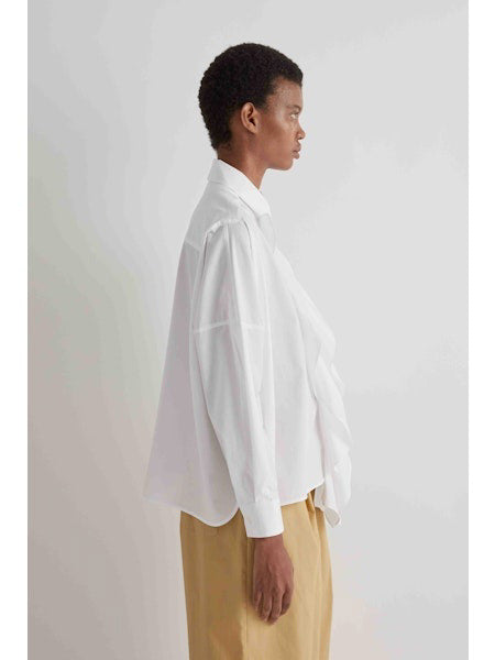 A person is facing away from the camera, wearing the MEIMEIJ - COTTON RUFFLE BLOUSE by MEIMEIJ with beige pants against a plain light background.
