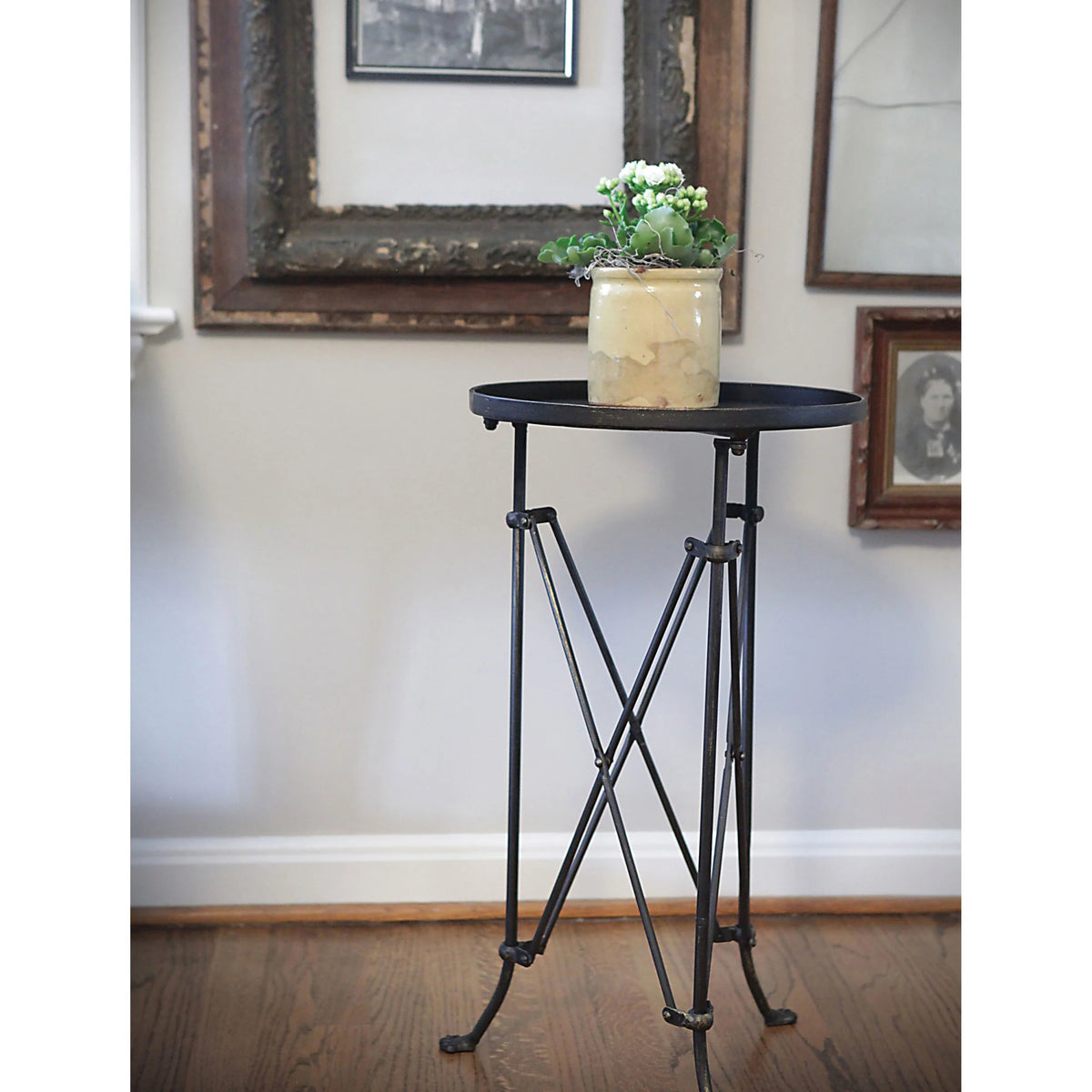 The CREATIVE COOP BRONZE FINISH METAL ACCENT TABLE is a small, round metal side table with a dark bronze finish, raised edge, geometric crisscross legs, and three vintage claw feet.