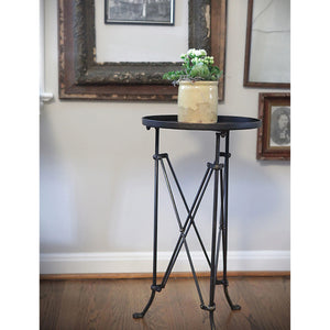 The CREATIVE COOP BRONZE FINISH METAL ACCENT TABLE is a small, round metal side table with a dark bronze finish, raised edge, geometric crisscross legs, and three vintage claw feet.