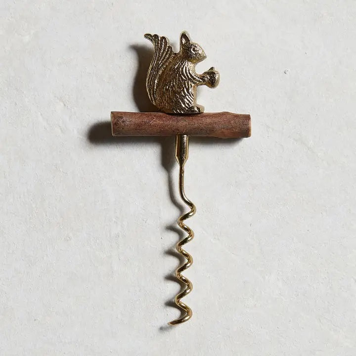 The BE HOME - SQUIRREL CORKSCREW by BE HOME, INC features a brown branch handle and a metallic squirrel with an acorn, adding woodland charm to your bar—perfect as a unique hostess gift. Shown on a light textured background.