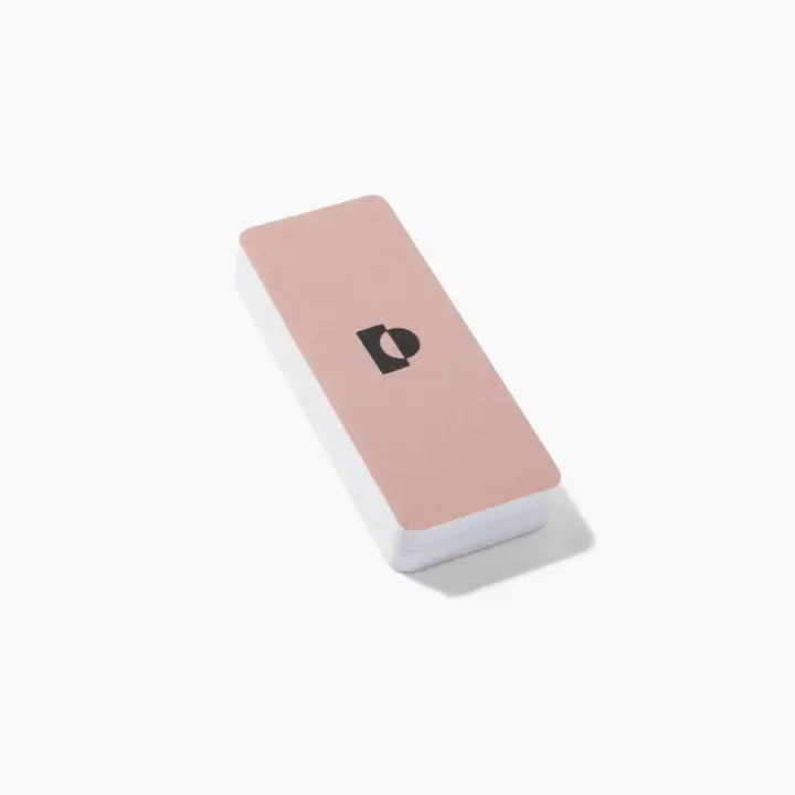 Introducing the TENOVERTEN - THE BUFF PLUS by TEN OVER TEN: a rectangular pink business card holder showcasing a sleek minimalist design. This elegant holder features a black geometric logo in the center, set against a white backdrop, reminiscent of the clean simplicity offered by the nail buffer. Captured against a plain white surface, the holder casts a delicate shadow to its right.