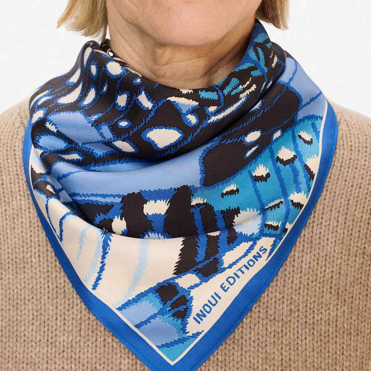 A close-up of the INOUI EDITIONS PAPILLON silk scarf in blue, featuring a smooth, shiny texture and abstract butterfly-inspired pattern in blue, black, and cream—a versatile accessory crafted in India by INOUI.