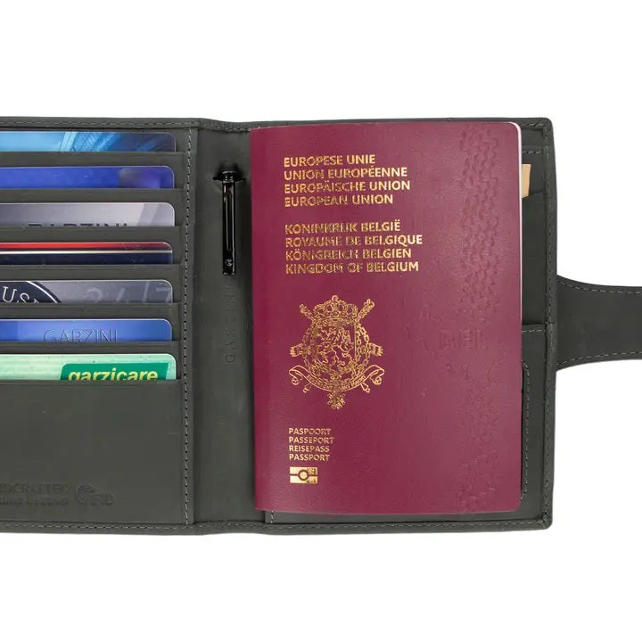 The GARZINI RFID-blocking leather passport holder in Carbon Black features multiple card slots, a pen holder, angled pockets, a transparent ID window, an Airtag compartment, and a snap-button closure flap.