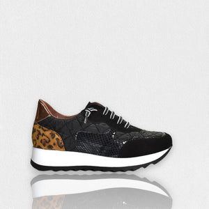 The CORDANI Lizzie Sneaker by CORDANI showcases a stylish leopard print design with brown and tan animal print panels, complemented by black and white laces and finished with a thick white sole featuring a black wavy tread, all set against a plain light background.