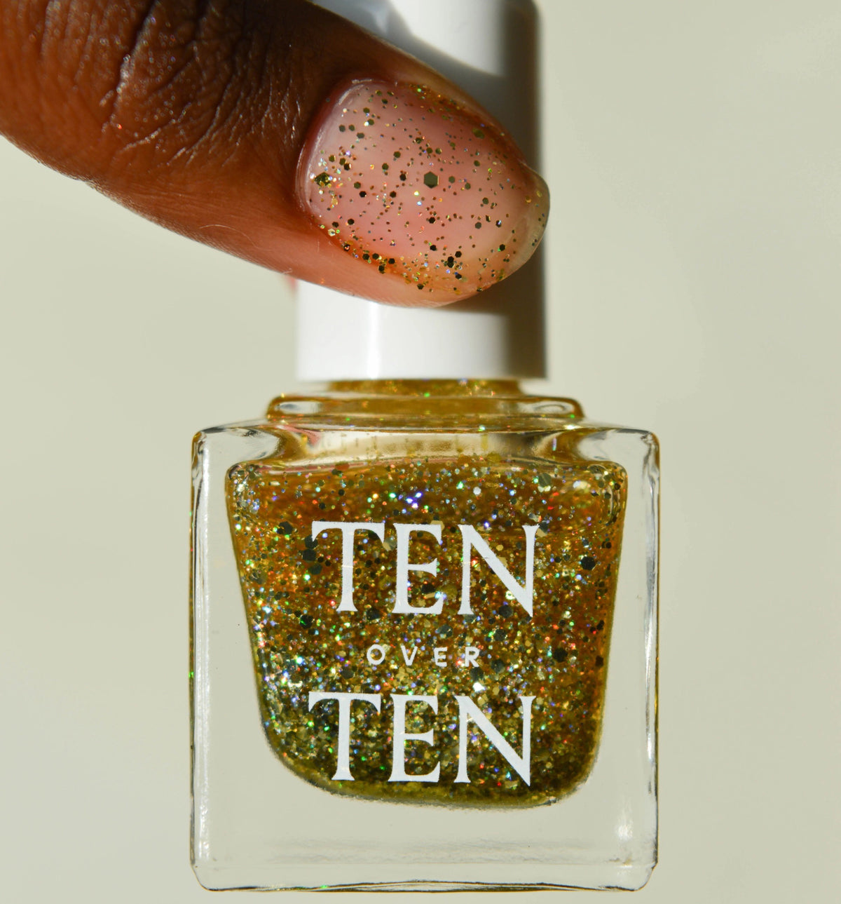 A glass bottle of TENOVERTEN - NAIL POLISH from the brand TEN OVER TEN, featuring a white cap and a dusty pink nail color. The front label displays "TEN OVER TEN" in white uppercase letters. This vegan, eight-free formula ensures both beauty and peace of mind. The background is plain and light-colored.