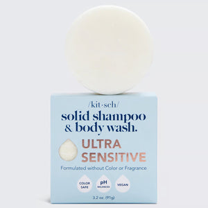 A round, cream-colored cleansing bar sits on a blue box labeled "KITSCH Ultra Sensitive Shampoo & Body Wash Bar." Packaging highlights include "4ocean Certified Cleanup Partner," "formulated without color or fragrance," "color safe," "pH balanced," and "vegan.