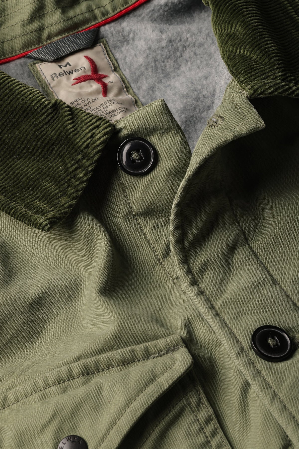 The RELWEN Pile-Lined Chore Coat in Palm Green is a stylish workwear jacket with a green quilted sleeve, olive-green collar and cuffs, and a soft gray fleece body with rugged lining, shown lying open on a white background.