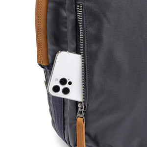 The TSD BRAND - MADRONE COATED CANVAS BACKPACK IN NAVY features brown leather accents, a spacious main compartment, a padded laptop sleeve with snap closure, and multiple zippered pockets on the inside flap.