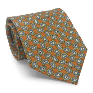 Introducing the PAGE SILK TIE IN ORANGE by BIRD DOG BAY. This expertly handmade New York tie features a vibrant orange base adorned with a repeating blue and yellow paisley pattern edged in green. With its pointed tip and solid white background, the PETER-BLAIR tie elevates classic design for a modern, sophisticated look.