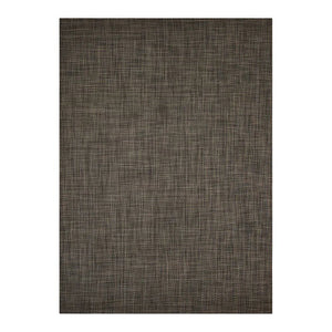 A wooden chair with a woven seat and simple backrest sits on the CHILEWICH - BASKETWEAVE FLOORMAT by CHILEWICH, made with recycled content, set against a plain white wall with white baseboards.