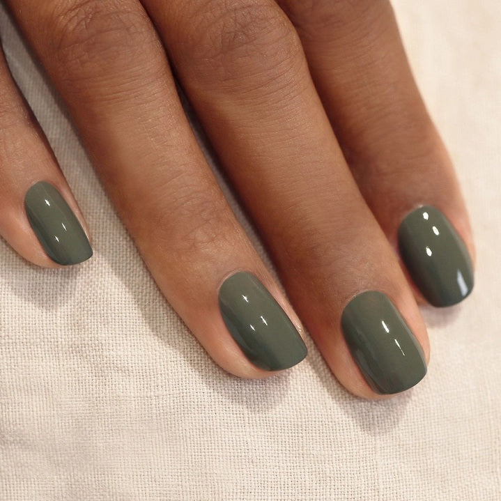 A bottle of MANUCURIST INC GREEN™ Nail Polish in Khaki, featuring a black cap and a label that reads “NAIL POLISH KHAKI, green, QUICK DRY INTENSE COLOR.” This vegan nail polish delivers quick-drying, intense color for a modern look.