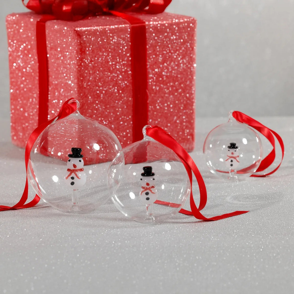 ZODAX SNOWMAN GLASS ORNAMENT: a clear 4-inch glass ball containing a small snowman figure, hung from a red ribbon.