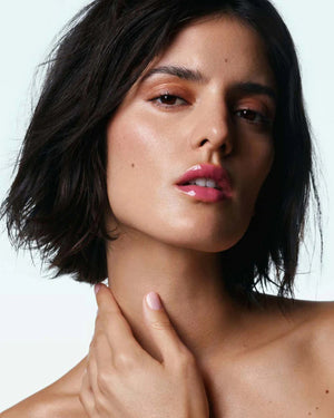 With radiant skin and short, dark hair, she exudes confidence, her lips subtly enhanced by U BEAUTY's Plasma Lip Compound in Orchid. Glowing makeup and a neutral background highlight her natural beauty.