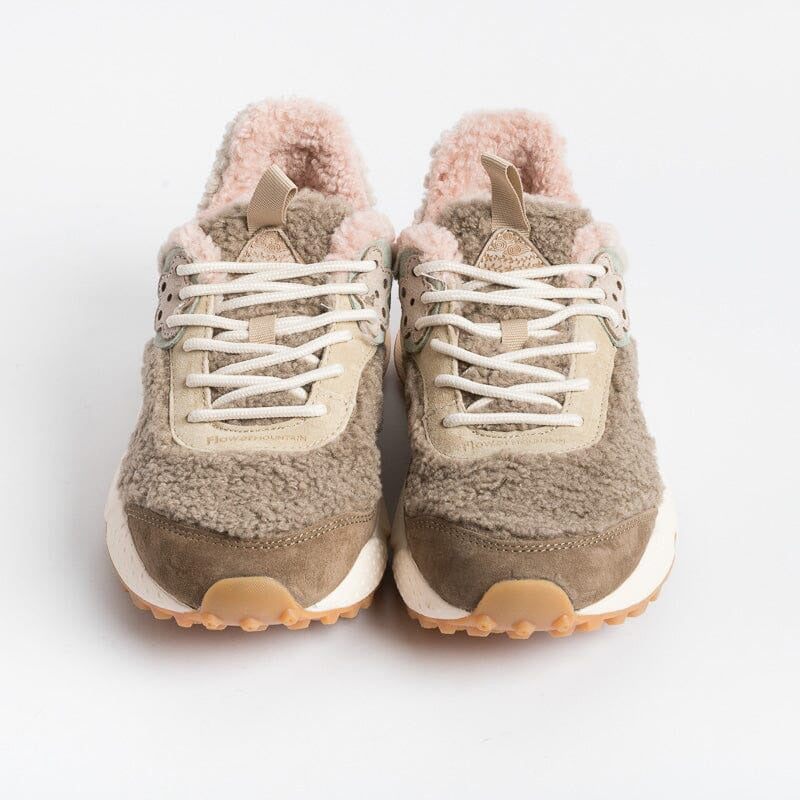 The FLOWER MOUNTAIN - KOTETSU SNEAKER by FLOWER MOUNTAIN/FALC USA is a stylish pair of beige and olive green shearling sneakers, featuring a textured, fluffy lining and trekking-style lacing in white. They come with a thick, white and brown patterned sole and an embroidered flower design on the side. Additionally, they have a pull tab on the heel. The sneakers are displayed against a plain white background.