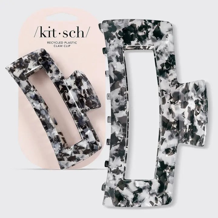 The KITSCH - Eco Friendly Jumbo Open Shape Claw Clip in Black is a rectangular hair accessory featuring a marbled black and white pattern, cutout center, and curved edges. Made from recycled materials, it is displayed on a light gray background.