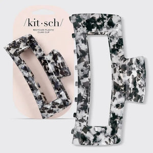 The KITSCH - Eco Friendly Jumbo Open Shape Claw Clip in Black is a rectangular hair accessory featuring a marbled black and white pattern, cutout center, and curved edges. Made from recycled materials, it is displayed on a light gray background.