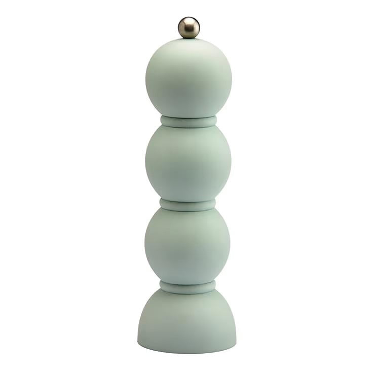 Green shelves showcase ADDISON ROSS LONDON's Scandi Bobbin Salt or Pepper Mill (23cm), a striped vase with white flowers, books, a bowl of red apples, and a vintage Campari poster in vivid green and red.