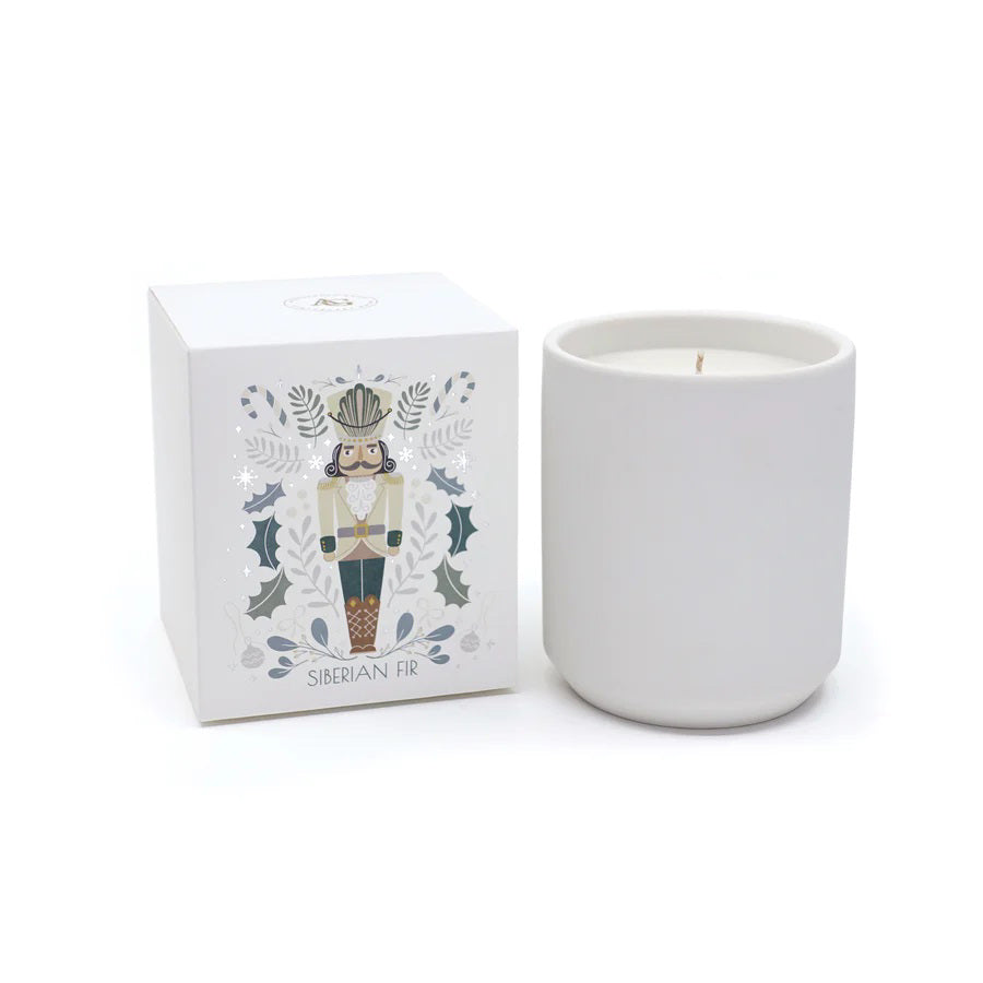 A plain NUTCRACKER SIBERIAN FIR CANDLE in a matte vessel sits next to its square box featuring a nutcracker illustration and holly motifs.