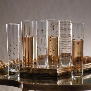 A set of six LA FETE GOLDEN DECAL CHAMPAGNE FLUTES by ZODAX, featuring tall, clear glasses adorned with decorative gold patterns such as stars, lines, and dots, showcased on a reflective surface. For details on dimensions or capacity, feel free to call the store.