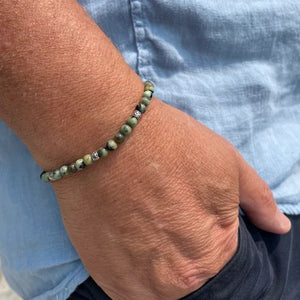 The STOLEN RICHES Formentera Bracelet in African Turquoise Stone features green and brown beads with silver accents on an adjustable brown cord, adding earthy elegance to any style.
