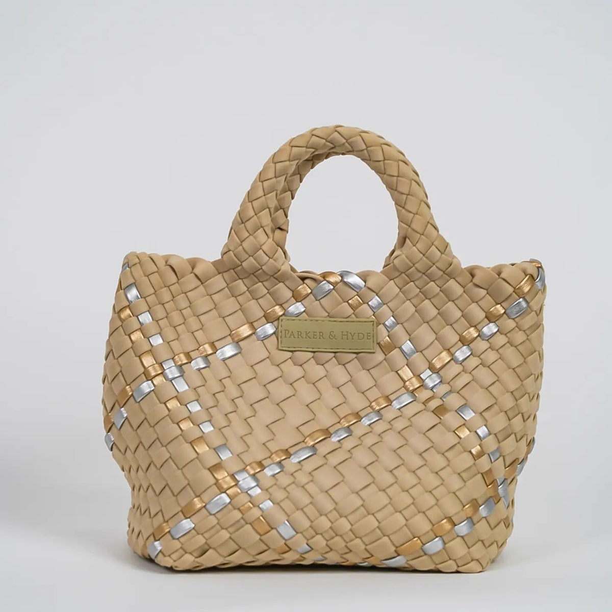 A woman with long brown hair, in a sleeveless cream knit top and blue jeans, holds a PARKER AND HYDE - MINI WOVEN TOTE BAG. The hand-woven tote by PARKER &amp; HYDE features a subtle checkered pattern with light blue accents.