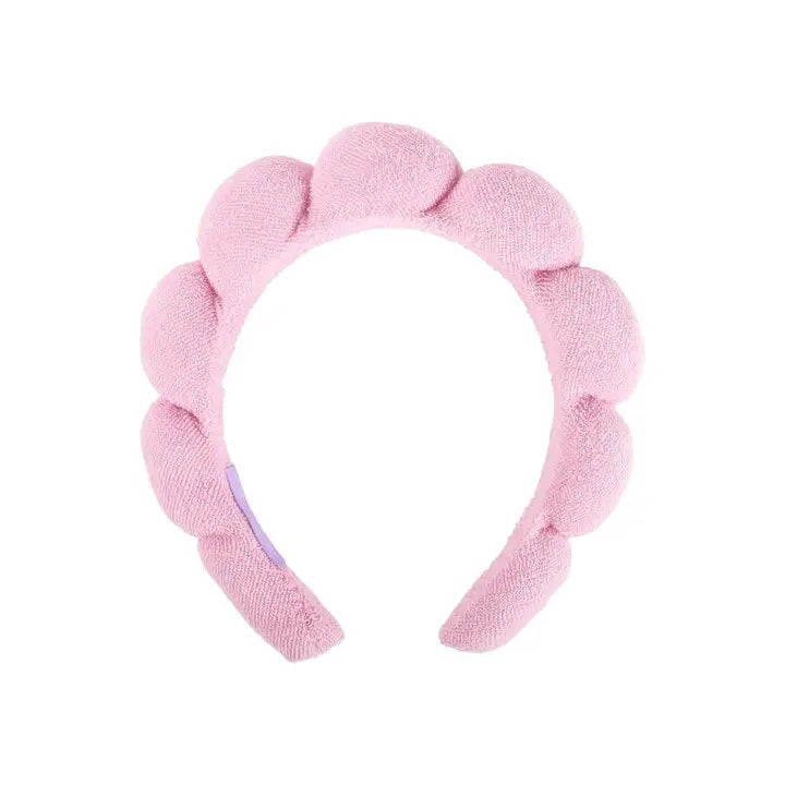 The CAIT &amp; CO PLUSH HEADBAND is a pink, scalloped hair accessory crafted from ultra-soft, textured material. Its design showcases a series of rounded, cloud-like shapes along the top, reminiscent of playful terry cloth headbands often used in a skincare routine.