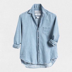 A light blue denim button-up shirt is displayed against a plain white background. The FRANK AND EILEEN - EILEEN RELAXED BUTTON UP CLASSIC WASH FAMOUS DENIM shirt features a relaxed fit, long sleeves rolled up to mid-forearm, a single chest pocket, and a slightly curved hem. Known for its bust-flattering button placement, the label inside reads "Frank & Eileen EST 1947.