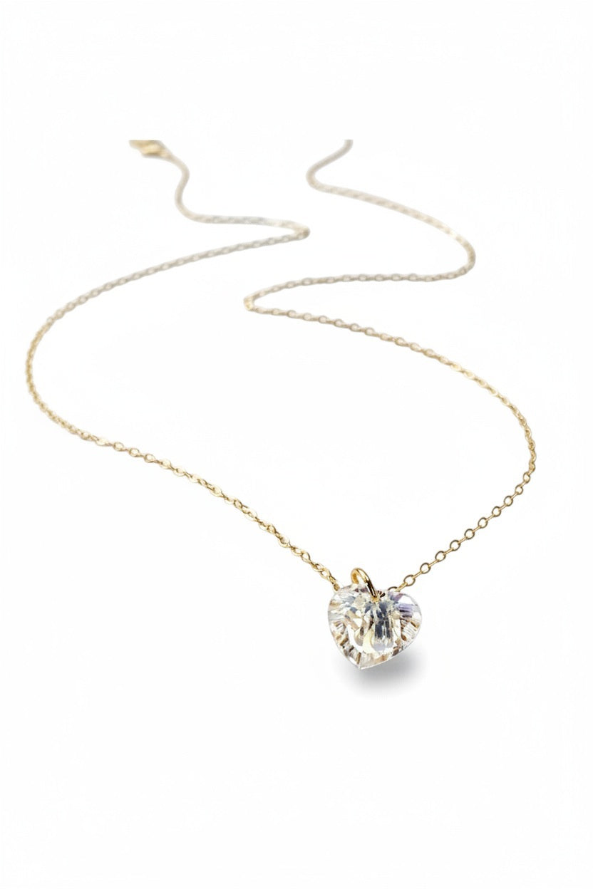 The VERDIER - AURORA CRYSTAL HEART NECKLACE from VERDIER features a sparkling crystal AB heart-shaped pendant suspended on a delicate 14k gold filled chain, shimmering against a white background.