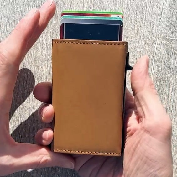 A closed GARZINI - SLIM TRIFOLD RFID-BLOCKING LEATHER WALLET WITH METAL CARD HOLDER AND COIN POCKET IN CARBON WITH RED sits beside a black "GARZINI" pen, both viewed from the side.