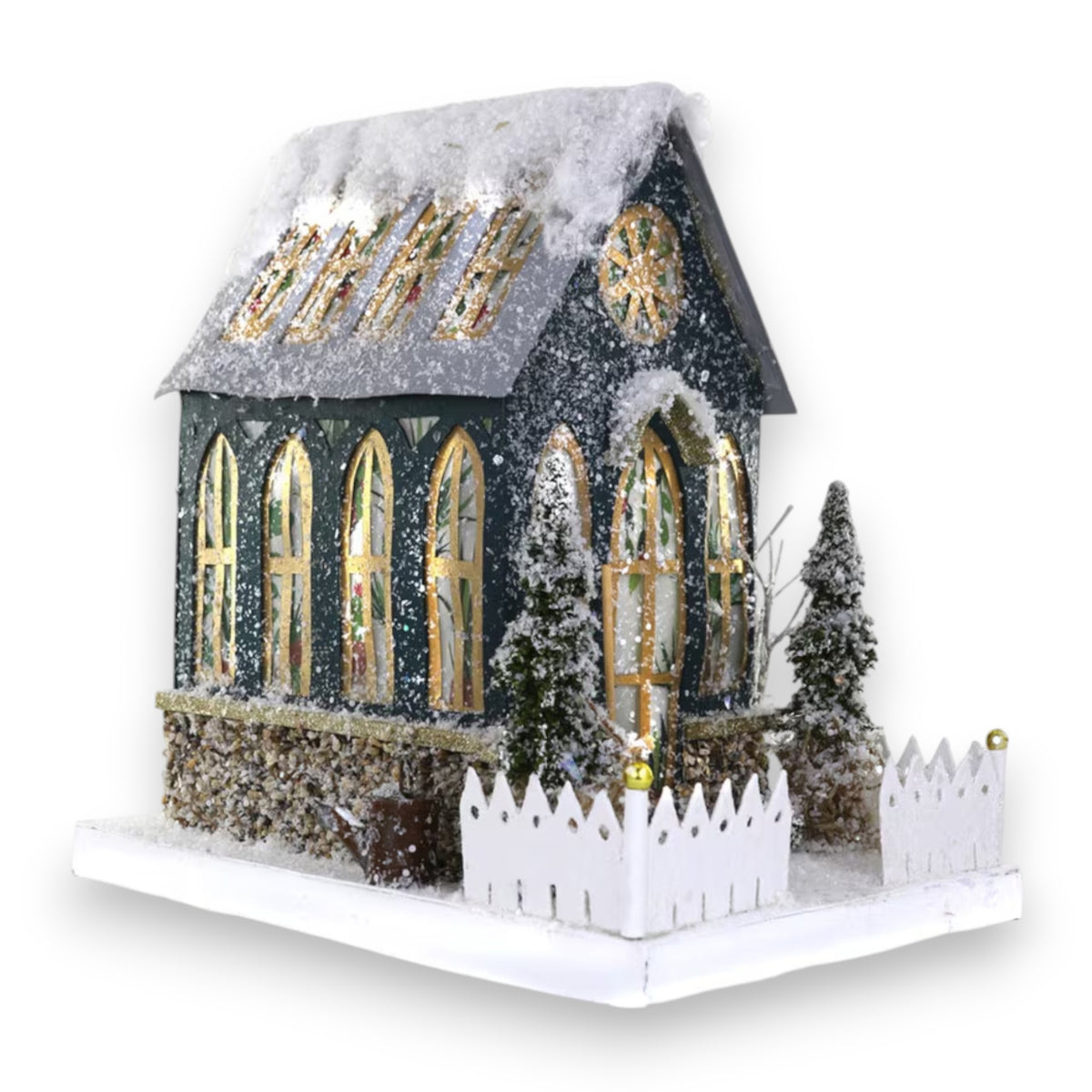 The GREENHOUSE HOLIDAY HOUSE by CODY FOSTER features a miniature snow-covered home with tall arched windows, a white fence, and small trees—an ideal collectible or thoughtful gift for design lovers.