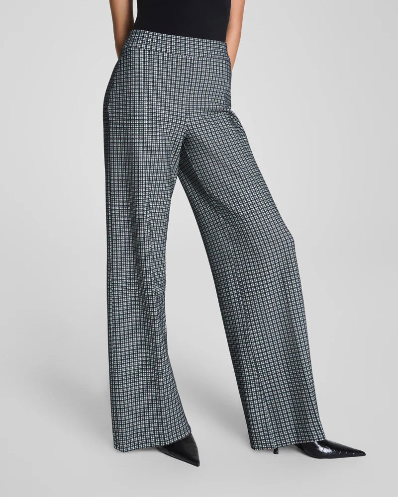 A person wearing SPANX Ponte Wide Leg Pant in Mini Collier, paired with a black top and black pointed shoes, stands with their back slightly turned.