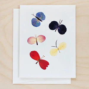 The PETAL PEOPLE PRESS - BUTTERFLY CARD by PETAL PEOPLE PRESS features five vibrant butterflies crafted from petals on a white background, accompanied by green leaves and office supplies—a charming botanical greeting card for any occasion.