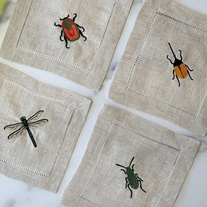 The EMBROIDERED INSECT COCKTAIL COASTER set by DOT AND ARMY includes four white reusable coasters, each edged in black and featuring a unique embroidered insect design—perfect for any gathering.