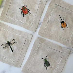 The EMBROIDERED INSECT COCKTAIL COASTER set by DOT AND ARMY includes four white reusable coasters, each edged in black and featuring a unique embroidered insect design—perfect for any gathering.