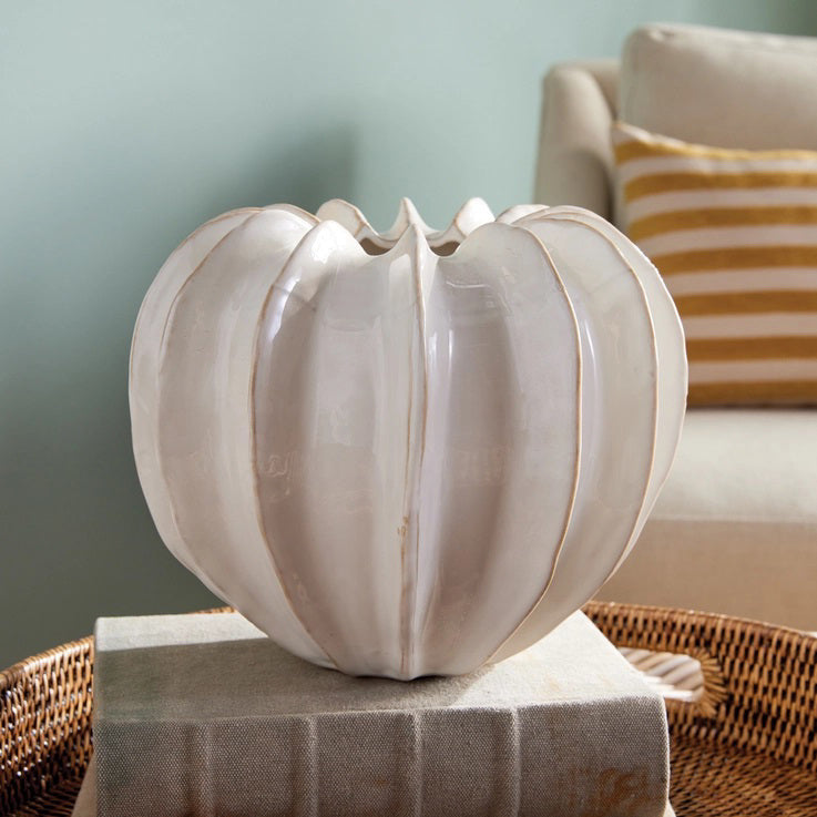 The NAPA HOME AND GARDEN - BLECKLYN POT is a white, glossy ceramic piece with a pumpkin-like form and pleated segments, featuring an artisan touch. Its uneven, scalloped opening evokes the essence of curated coastal-inspired design.