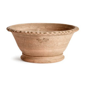 The NAPA HOME AND GARDEN - WAKEFIELD ALVENA FORCING POT holds tall white orchids with green leaves and buds. The beige handmade terracotta pot is shown on a white background with the caption "WITH DROP-IN K112W" below.