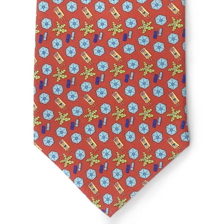 A rolled-up red necktie featuring a repeating pattern of pink beach umbrellas, yellow-green palm trees, and blue beach towels, the Peter-Blair Sunscreen Silk Tie by Bird Dog Bay is handmade in New York and finished with the signature Peter-Blair woven label.