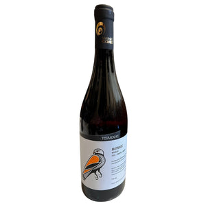 A bottle of TSIAKKAS ‘MOUKLOS’ MAVRO 2024 red wine with a label featuring an illustration of an orange and black bird, sitting on a white table in a restaurant.