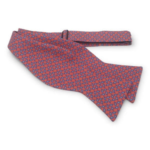 A self-tie, adjustable neck bow tie from Bird Dog Bay, the PETER-BLAIR New Pine Silk Bow Tie in Pink and Blue features a repeating blue and pink pattern, laid flat on a white background. This handmade bow tie is crafted from printed silk for a refined and elegant finish.