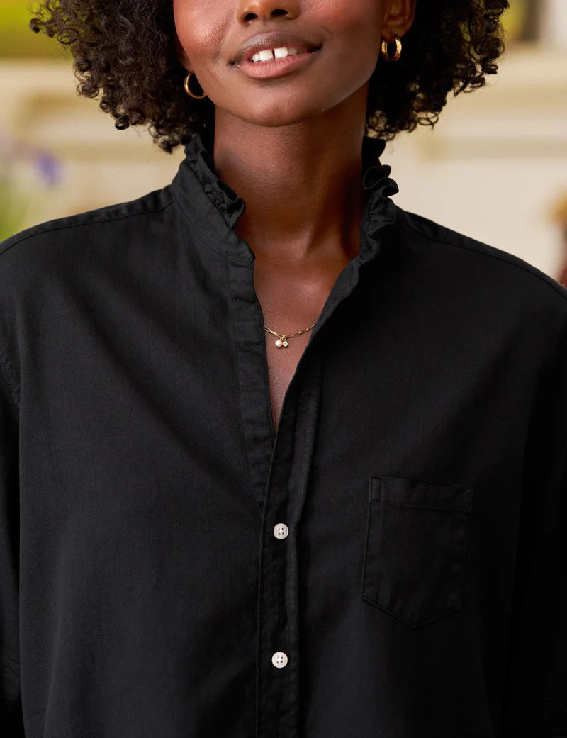 The FRANK &amp; EILEEN Ruffle Eileen Ruffle Collar Button Up Shirt in Famous Denim Blackout features long sleeves, white buttons, a single chest pocket, and a ruffled collar, shown laid flat against a white background.