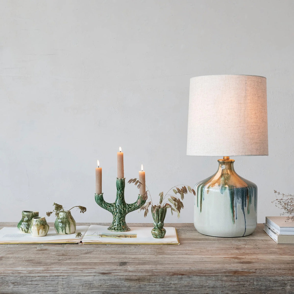 The CREATIVE COOP Stoneware Table Lamp features a textured beige linen shade and a ceramic base with artisan green and brown drip glaze over cream.