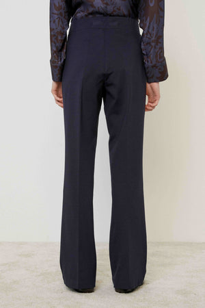 A person in MEIMEIJ PULL ON PONTE TROUSER PANT, a patterned long-sleeve blouse, and black shoes stands on a light carpet against a plain wall, highlighting this versatile MEIMEIJ wardrobe essential with a tailored look.