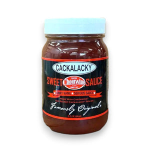 A person brushes savory barbecue sauce onto the burgers sizzling on the grill, holding a jar of CACKALACKY - CHEERWINE SWEET SAUCE in their other hand. This scene of Southern cuisine unfolds against the backdrop of a grassy outdoor setting.