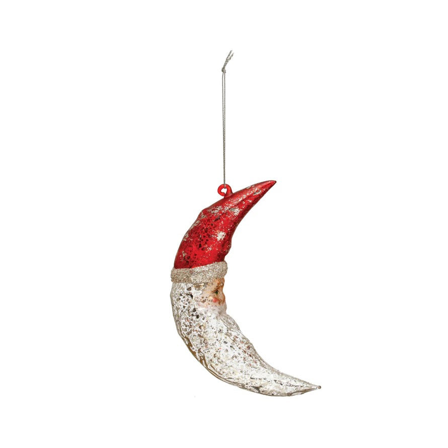 The CREATIVE COOP HAND PAINTED MERCURY GLASS SANTA MOON ORNAMENT features a crescent moon shape with a red tip, silver glitter accents, and a hanging string—perfect for adding festive charm to your Christmas tree.